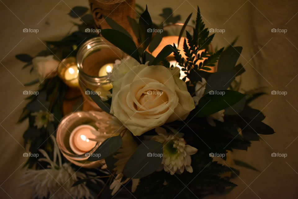 Top view of a romantic wedding center piece with rustic greens and eucalyptus, natural wood, white flowers and romantic candle light on neutral background. 