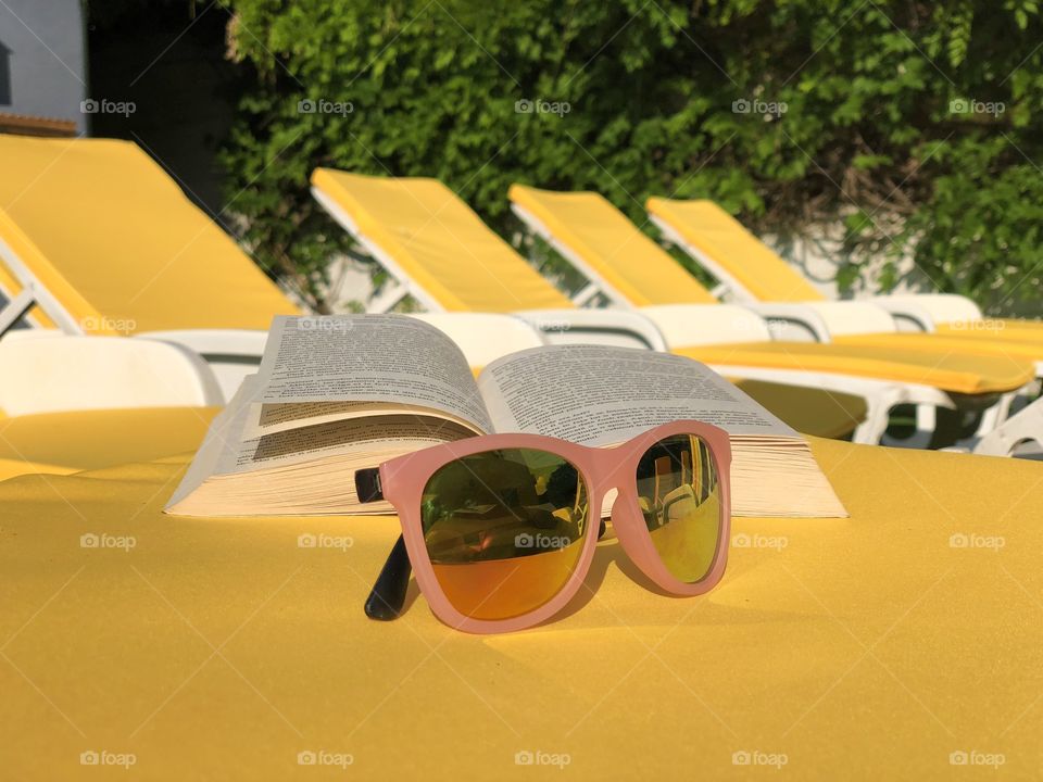 Pink sunglasses and a book placed on a yellow sunbed with many yellow sunbeds in the background