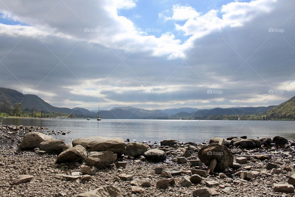 The rocky shoreline of Derwent Lake Cumbria, with heavy rain clouds above looming over the scenic hillside 