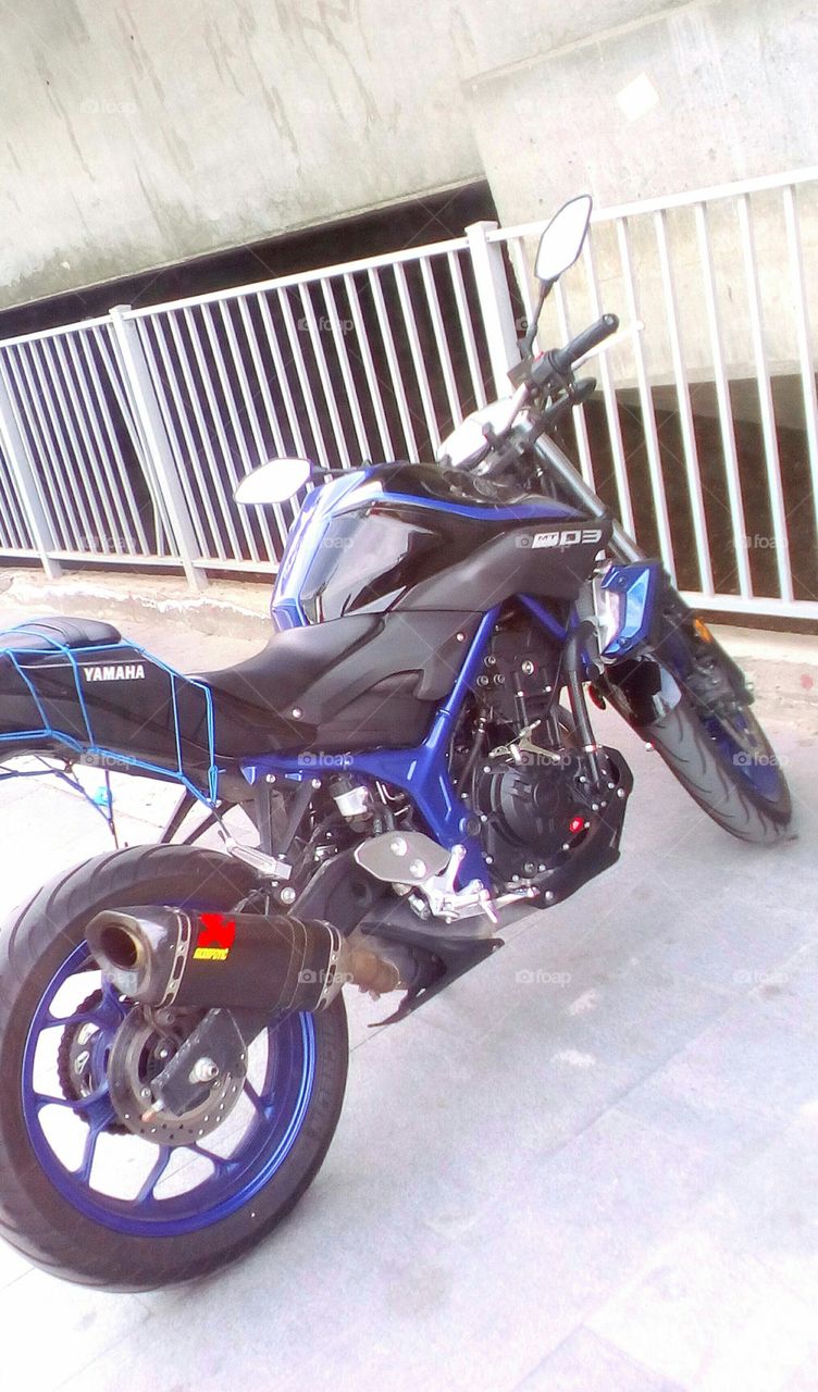 Blue indigo Yamaha brand motorcycle
parking in street on grey urban pavement
near iron fence in daylight