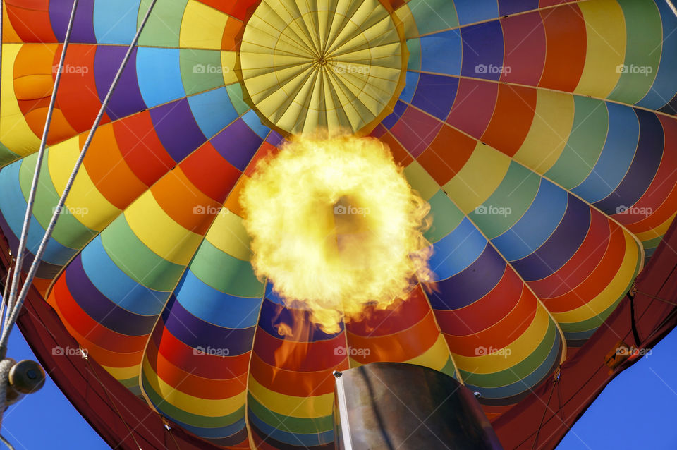 Looking up into a hot air balloon from the basket below as the pilot heats the air and the balloon takes off