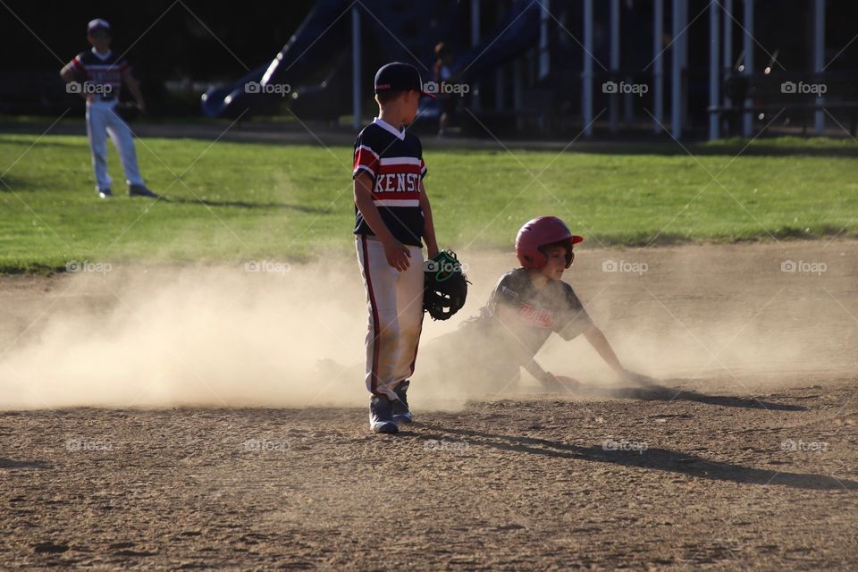 Baseball player slides second base with cloud of dust surrounding him