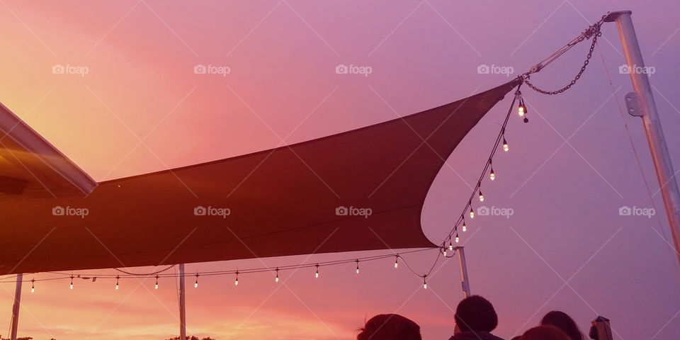 Awning with Edison lights strung over a bar deck at Beach restaurant in NC. sunset silhouette