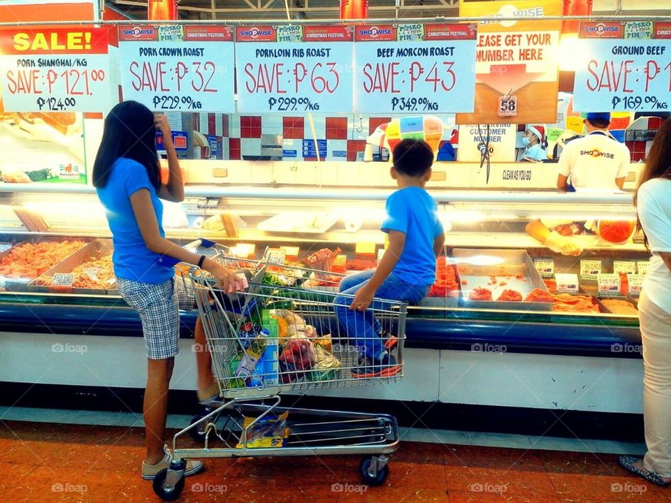 Siblings wait by their grocery cart as their mom shops for their food