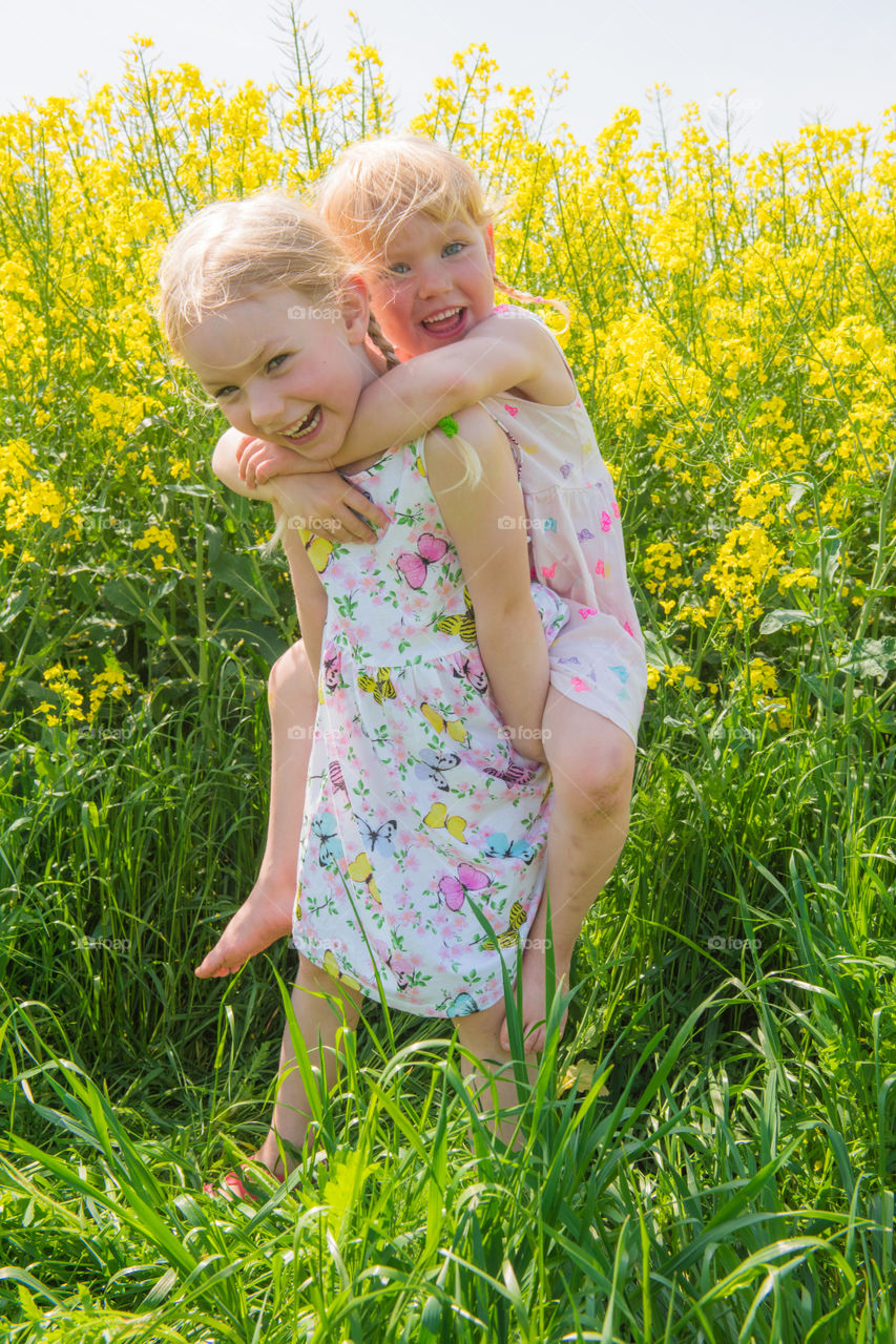 Happy girl carrying her little sister in flower field