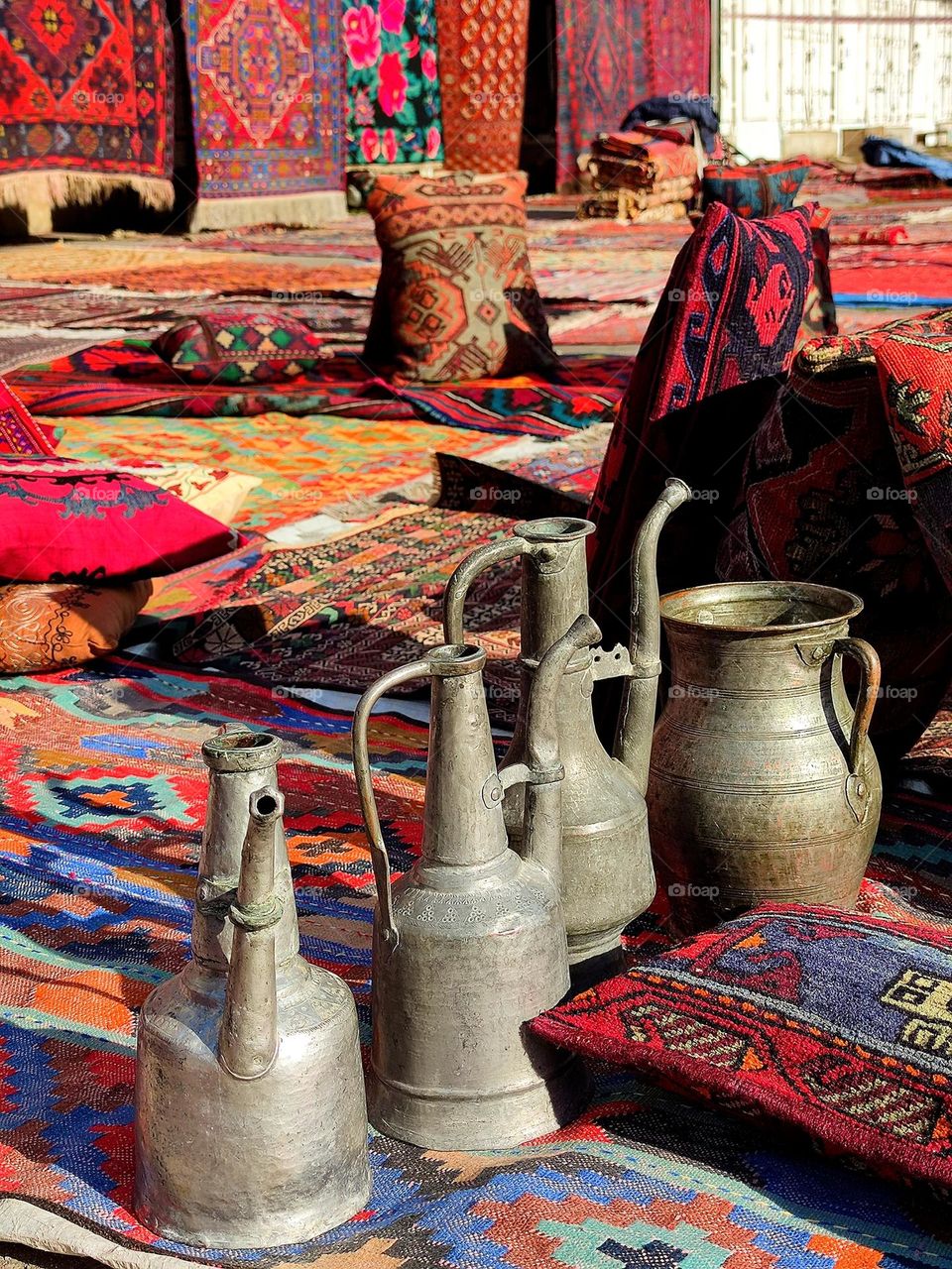 East market.  Antique metal vessels stand among bright handmade carpets.  Eastern fairy tale