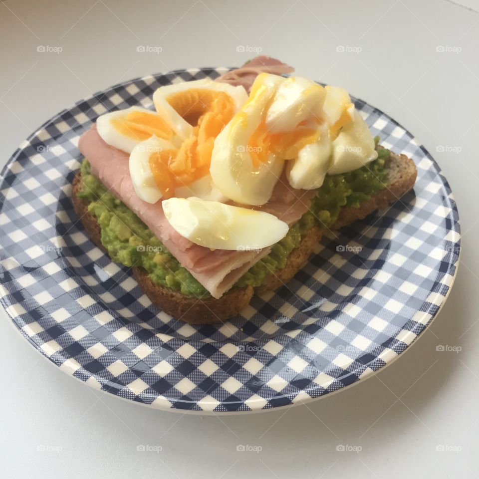 Eggs ham and avocado on a slice of bread or toast on a blue and white checkered plate 