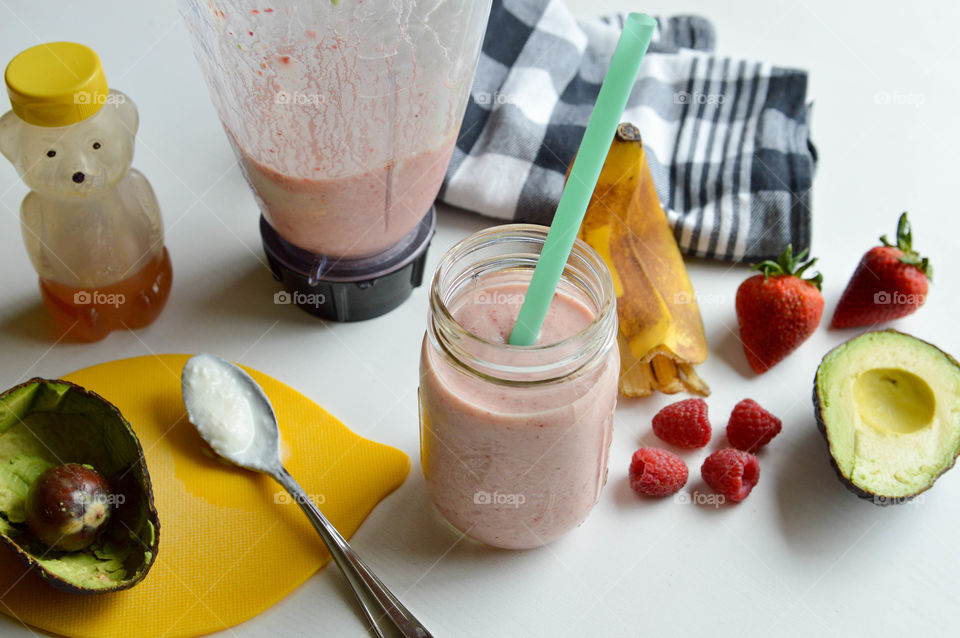 Fresh fruit smoothie in a glass with banana peel, avocado, raspberries, strawberries, and honey