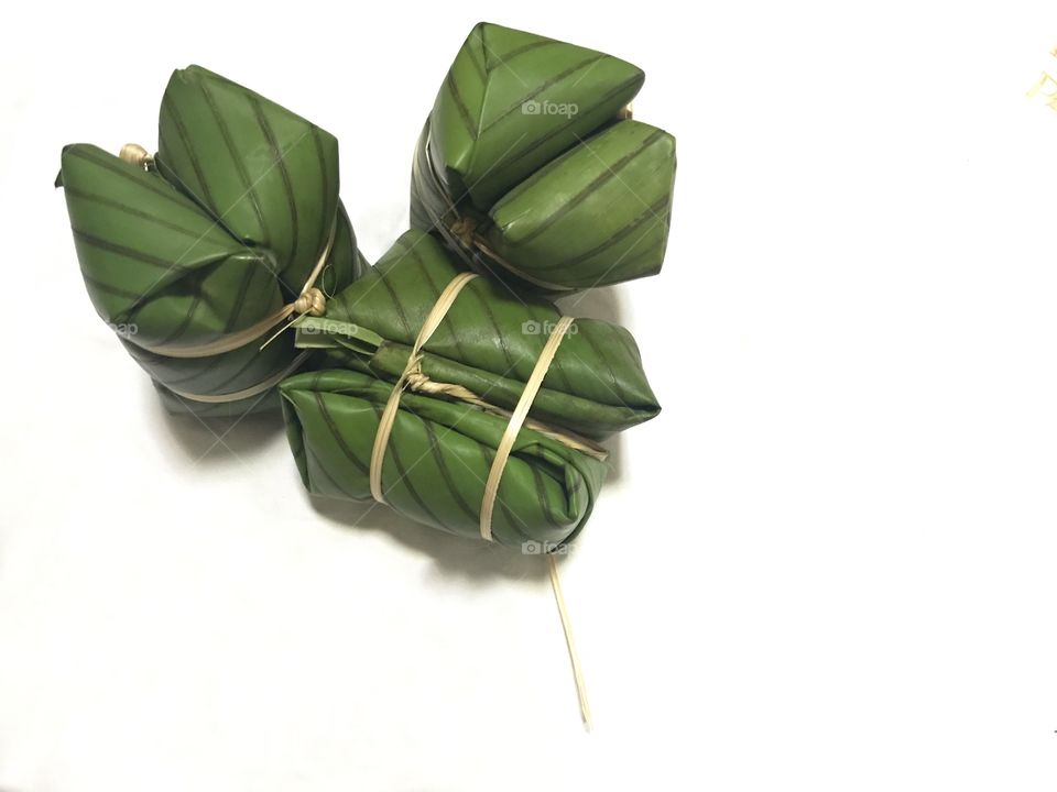 raw thai traditional dessert which called khao tom mud in thai or bananas with sticky rice which are wrapped with green banana leaf and flat thin bamboo strip on white background