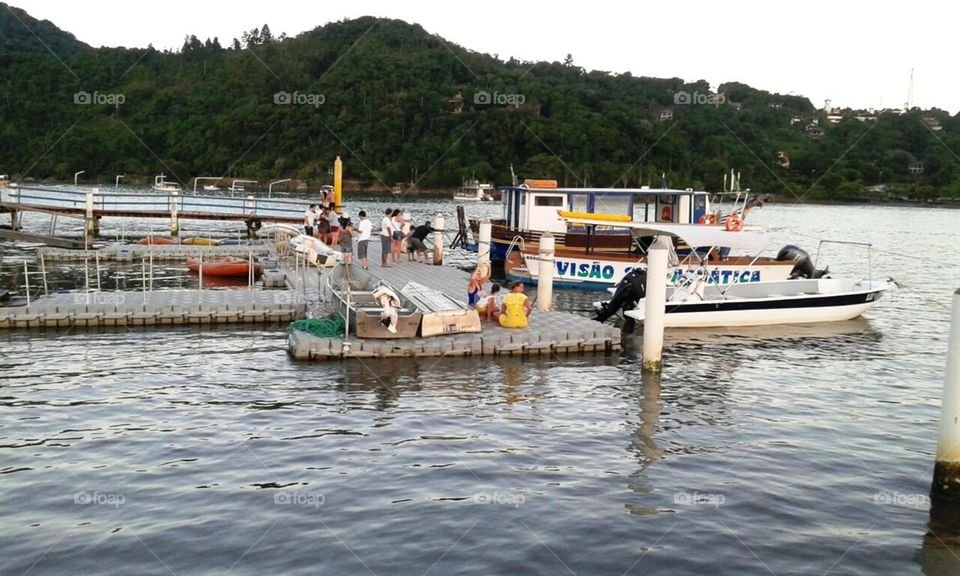Pessoas curtindo um feriado à beira de barcos e paisagem à tarde.