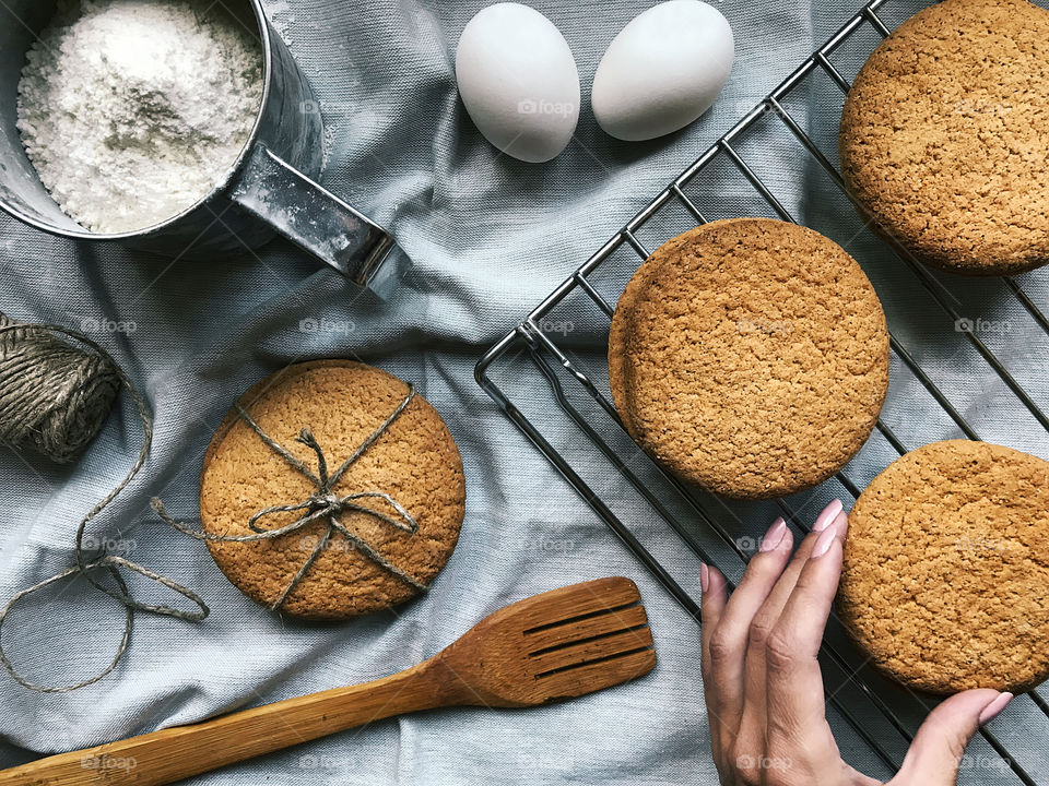 Female hand holding a freshly baked homemade cookies on the rustic table with ingredients for cooking 
