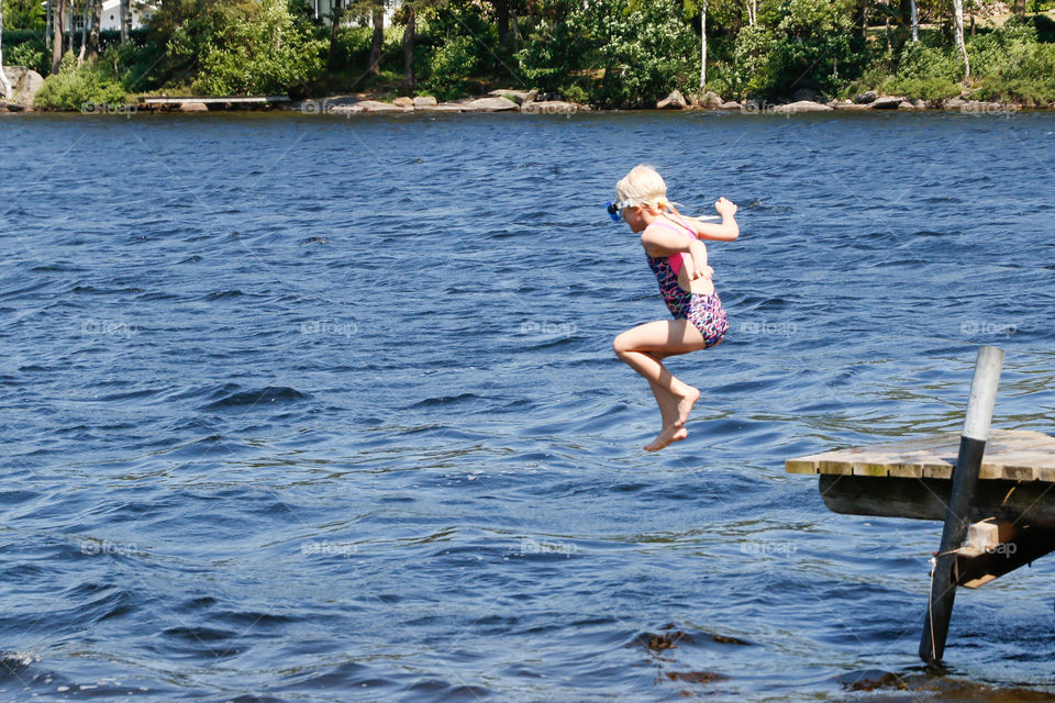 A young girl jumping into the lake from a wooden jetty 
