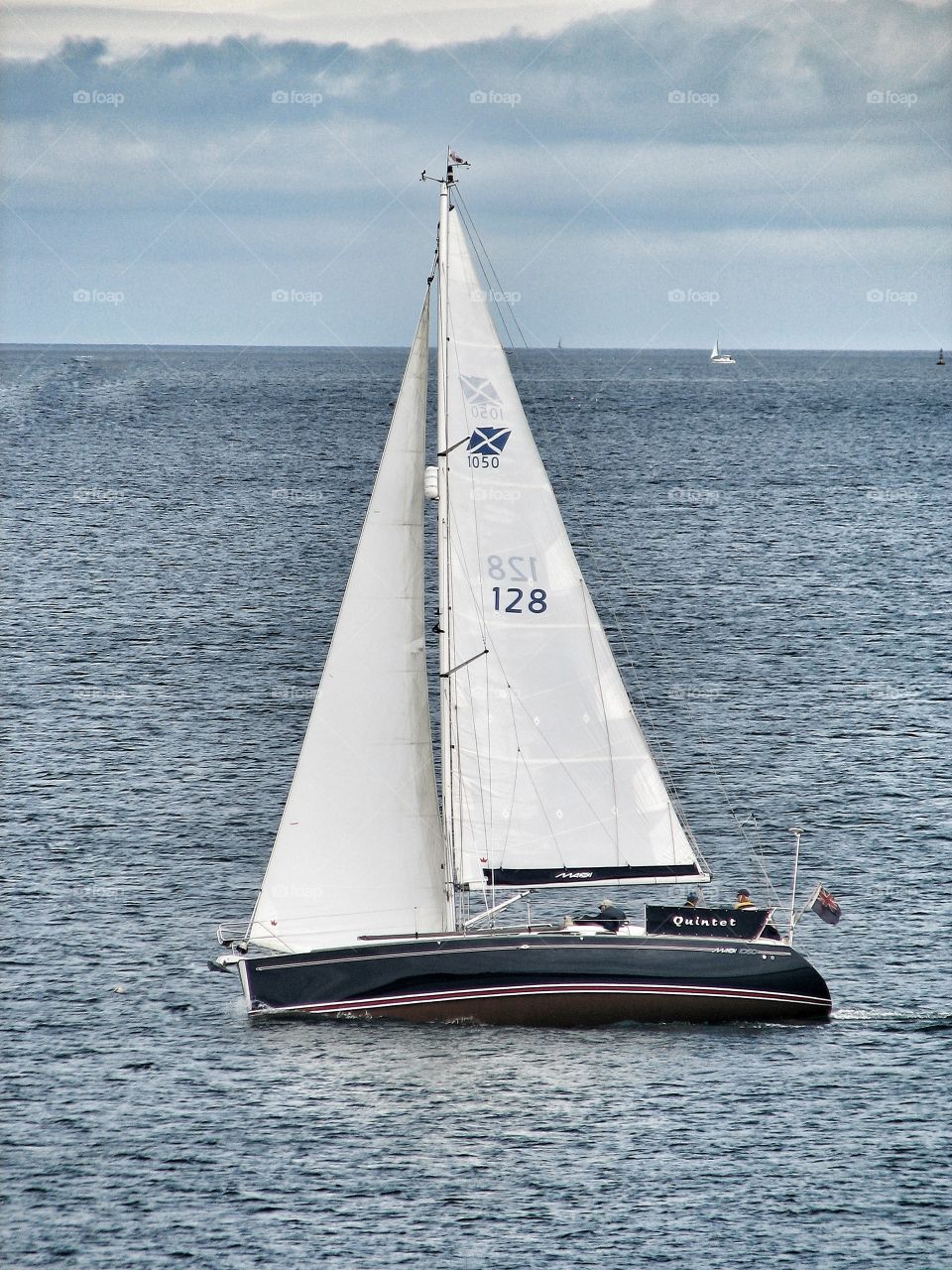A sailing boat with a large sail corners on the ocean.