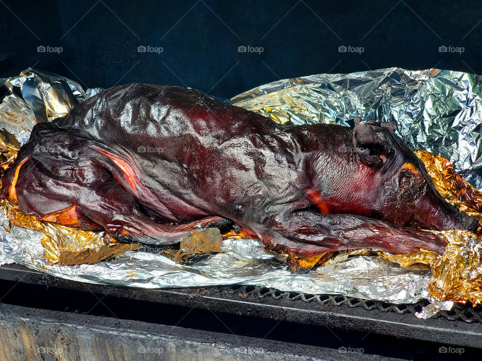 A roast pig sits atop a smoker after 16 hours of slow cooking