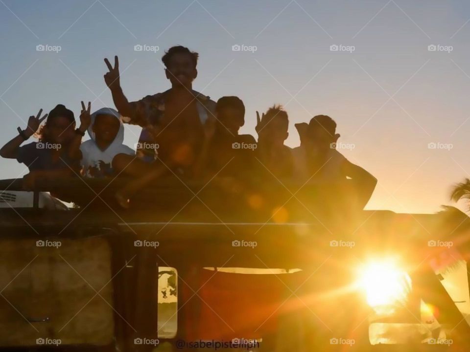 Group of boys posing on top of car under sunset