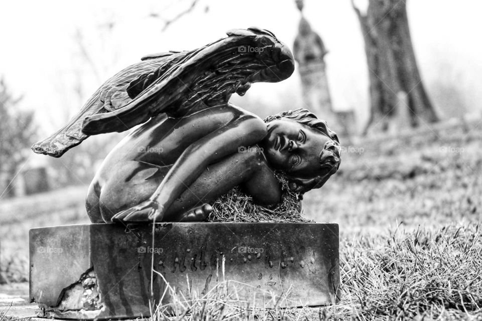 Black and White photo of an angel figure statue on top of a grave in an old cemetery