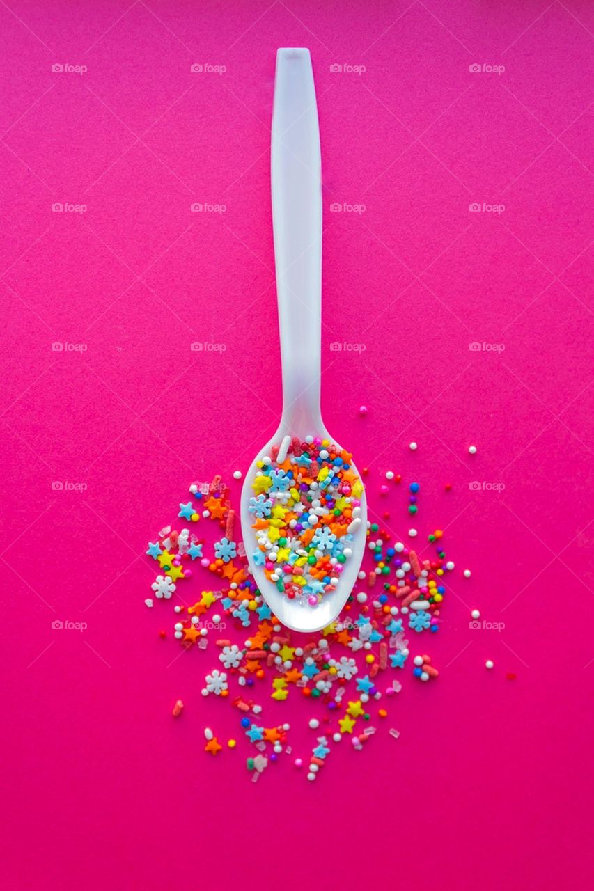A spoonful of sugar and sprinkles against a vibrant pink background 