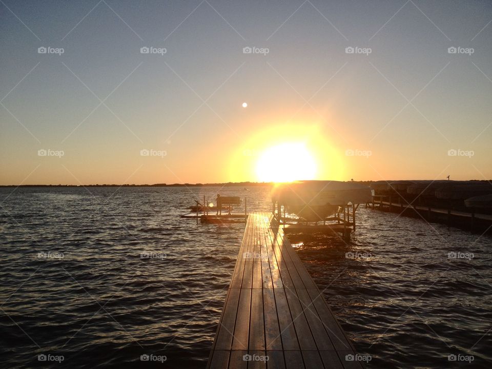 Gorgeous golden bright yellow sun is setting off in the distant horizon behind wooden dock!