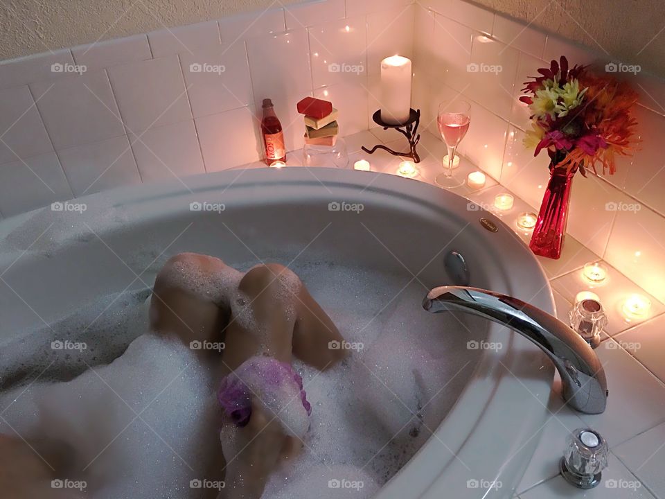 A woman relaxing in a romantic bubblebath surrounded by candlelight.