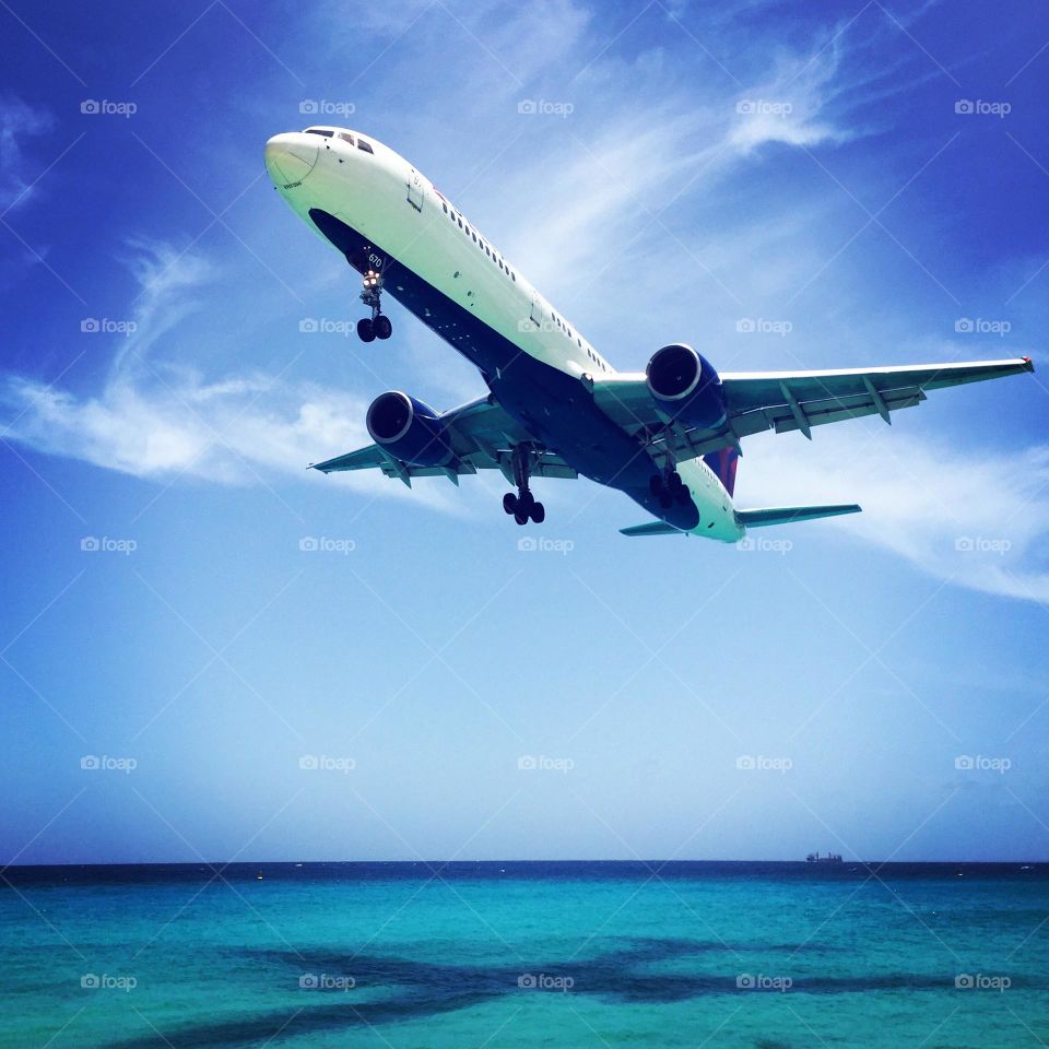 Plane flying over ocean, plane landing in St. Martin, Maho Beach in St. Maarten, flying to an island, flights to St. Martin, big plane flies over open water 