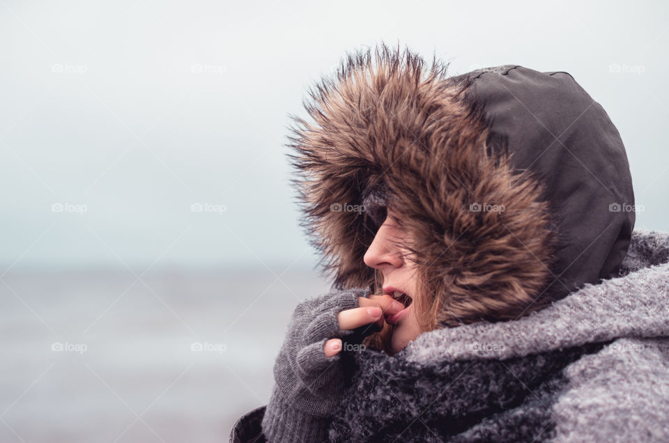 Side view portrait of a beautiful girl in warm clothing eating snacks at the beach.