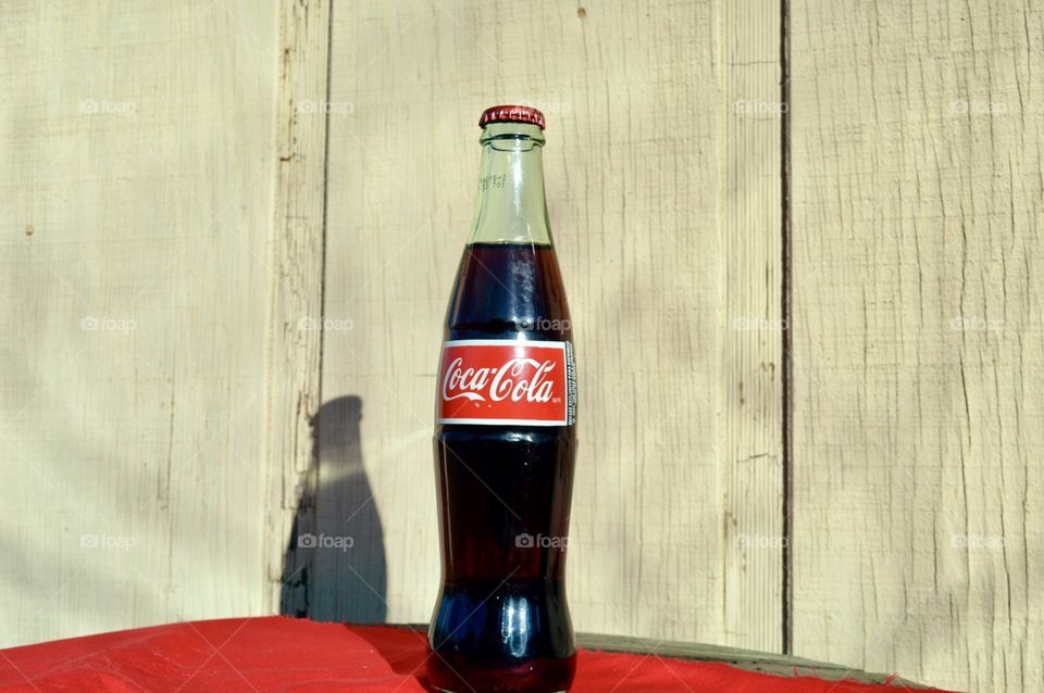 A bottle of Coca-Cola on a table top with a red linen and rustic background