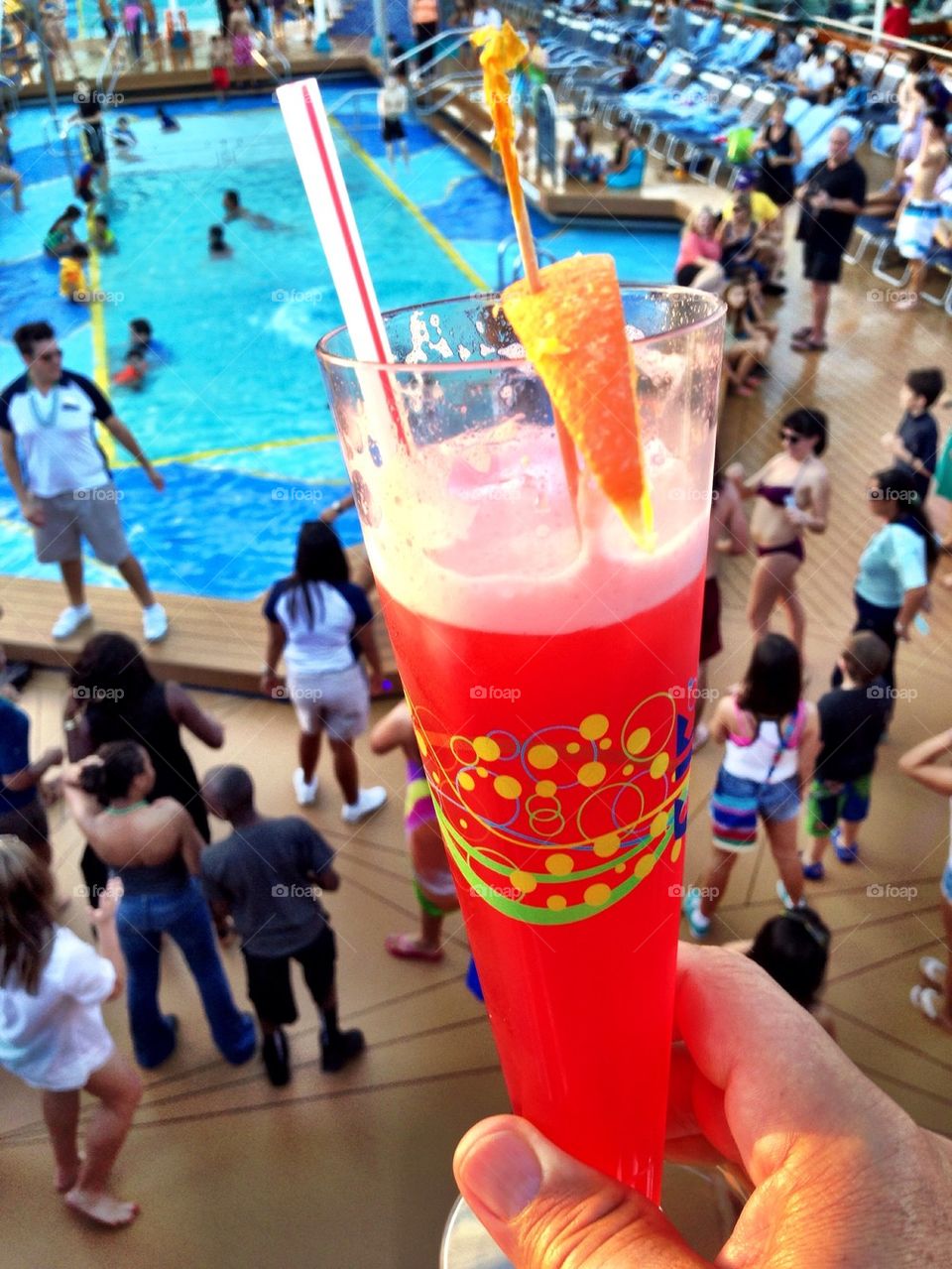 Man holding drink with people dancing on cruise ship deck