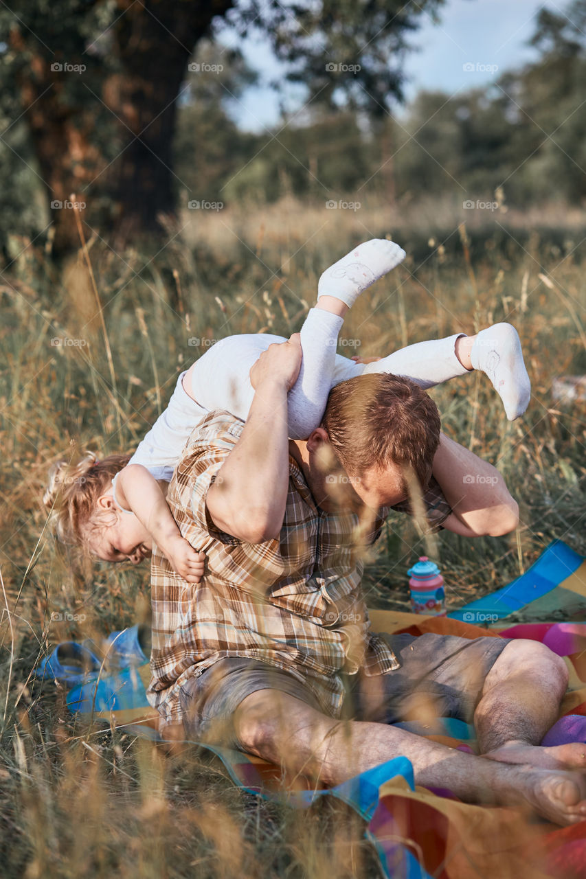 Father playing with little girl on a meadow, close to nature. Parents and children sitting and playing on a blanket on grass. Candid people, real moments, authentic situations