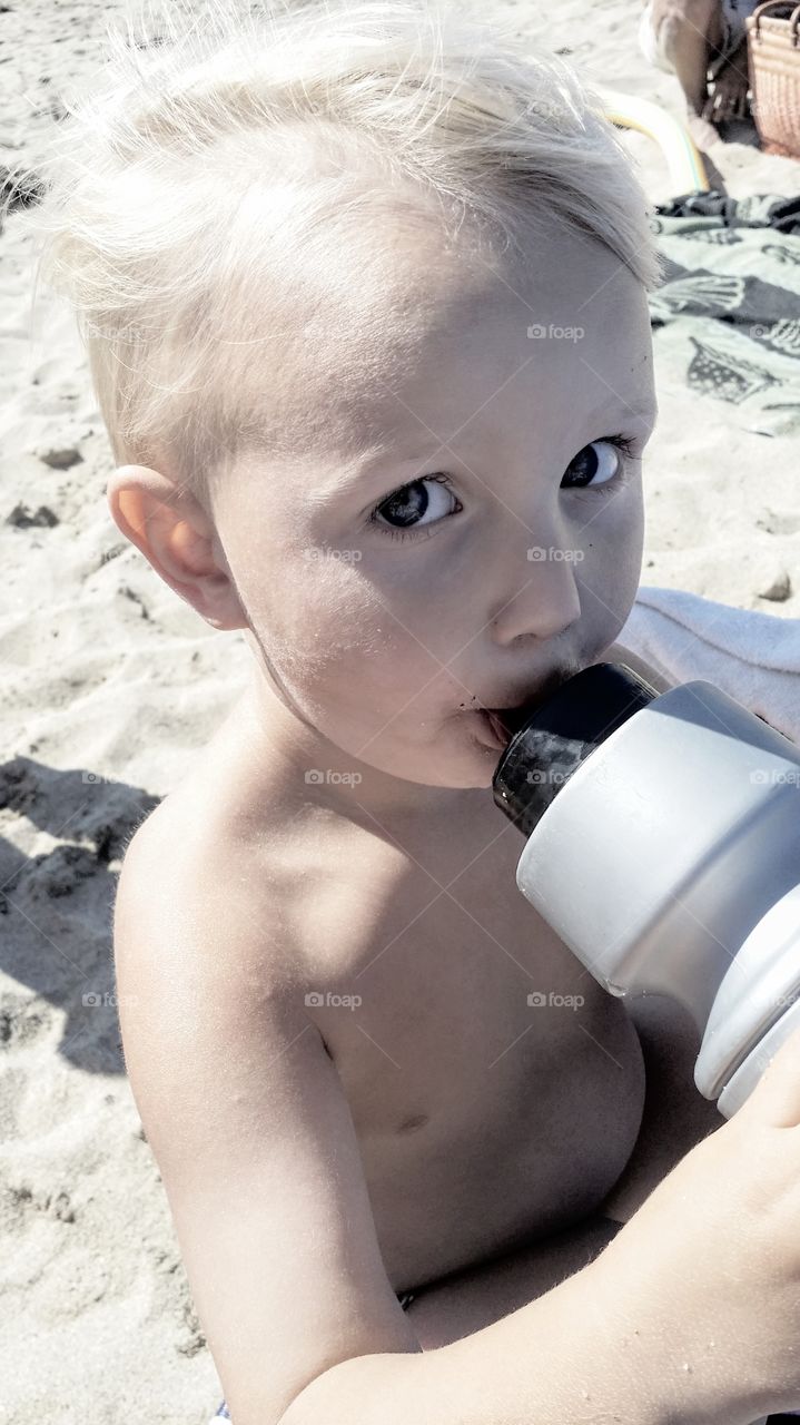 Boy drinking from water bottle at the beach