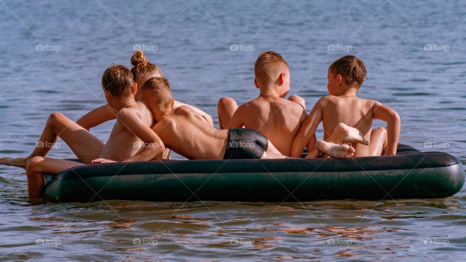 children swim on a mattress on the water