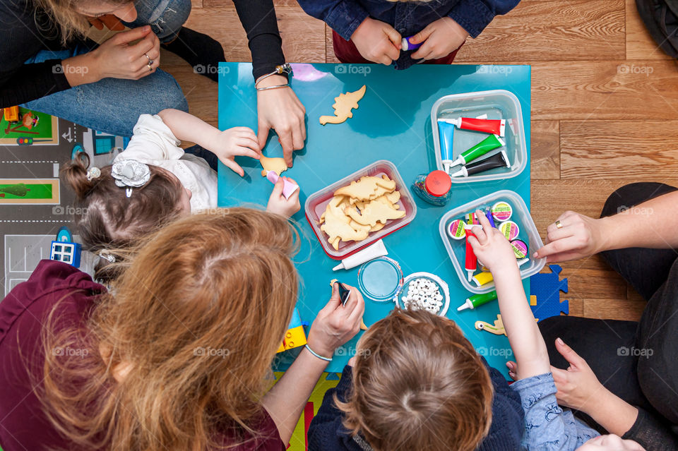 Children with parents having fun decorating home baked dinosaur cookies.