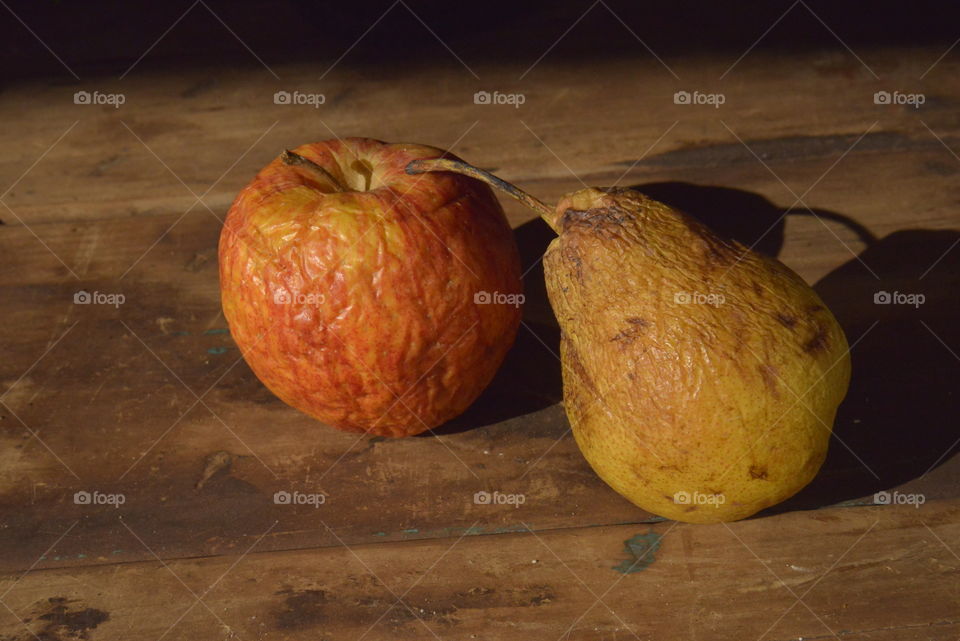 Two rotting fruits, a pear and a qpple, covered in wrinkles and spots.