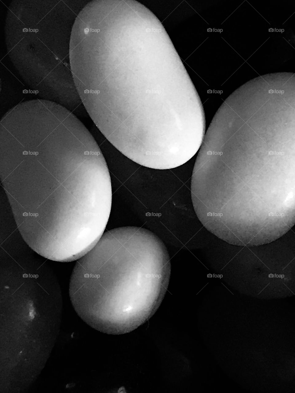 A monochromatic picture of jellybeans with the exposure adjusted so just the four white jellybeans are visible creating interesting shadows and making the beans resemble pearly-white, rounded stones. 