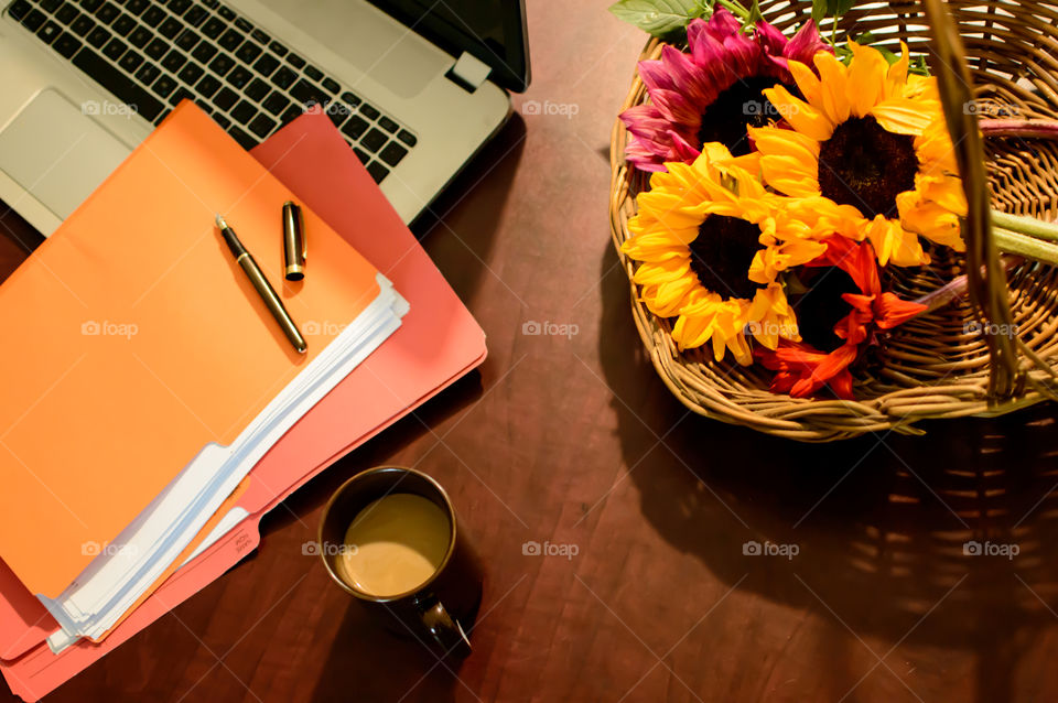 Bright Sunflowers on desk with laptop, files with paper, fountain pen and cup of coffee elevated view conceptual work life balance tranquil business scene