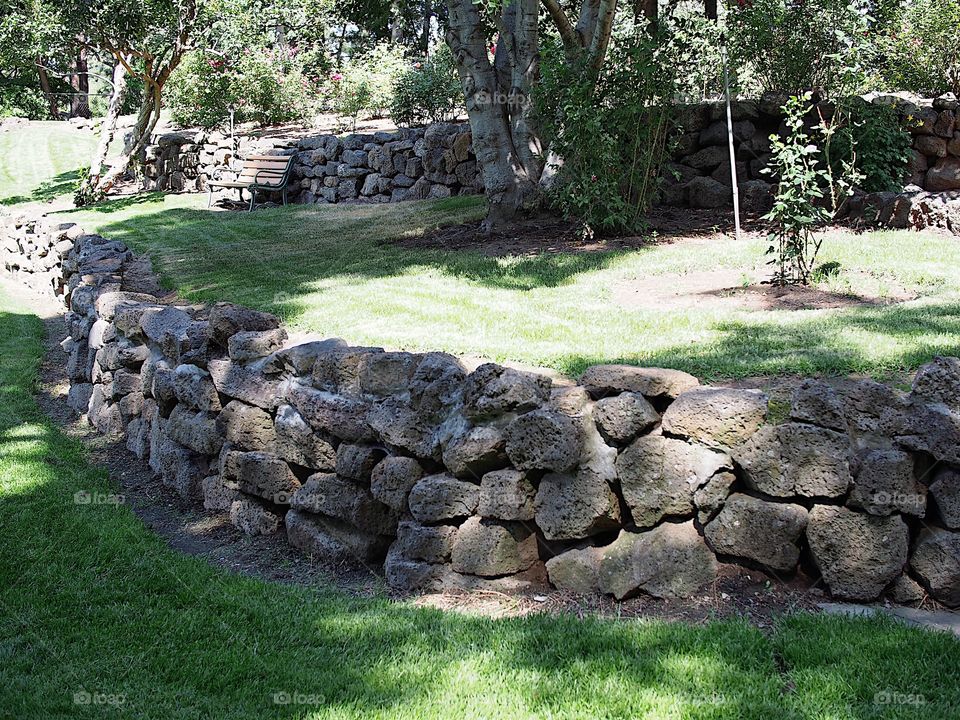Multiple tiers with rock walls of different growth from grass to flowers and trees as well as a park bench in Pioneer Park in Bend in Central Oregon on a beautiful sunny summer day.
