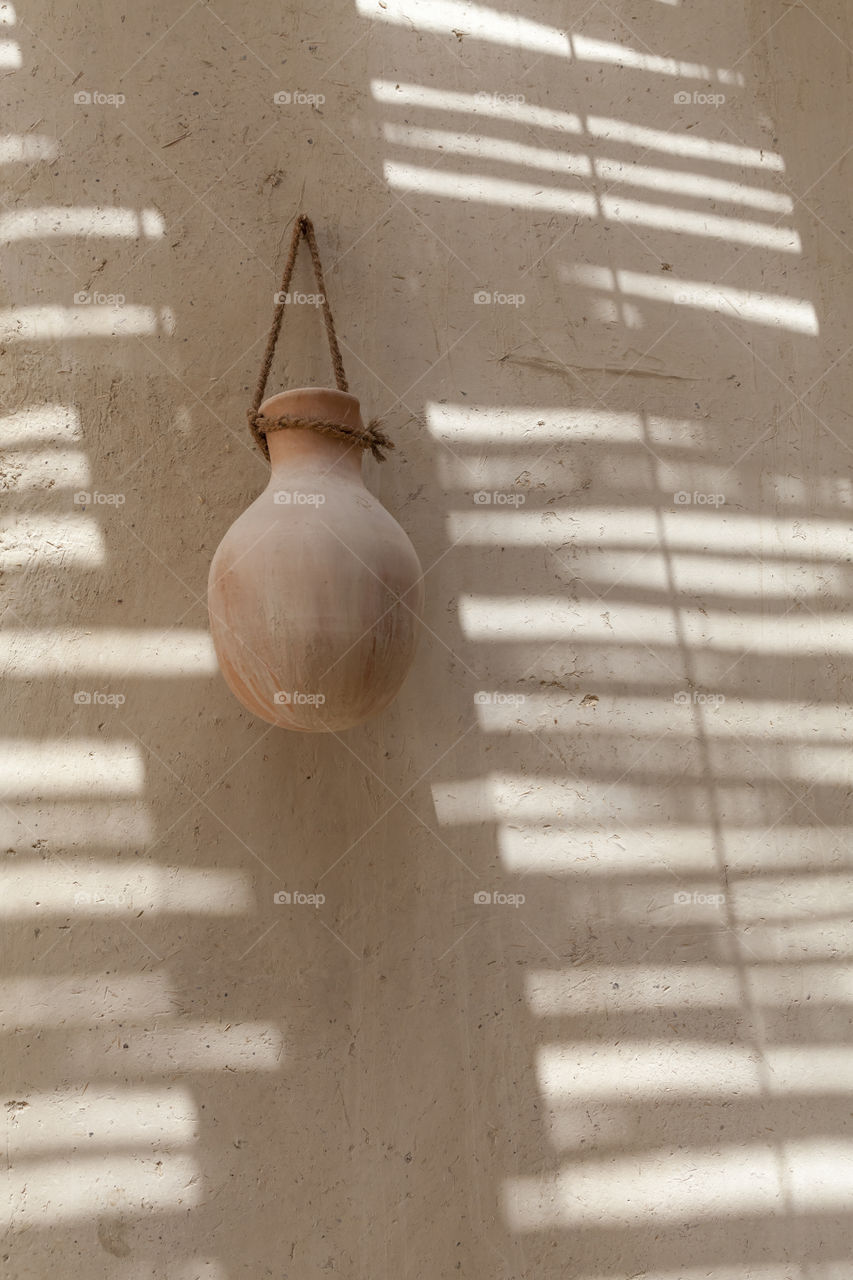 Brown clay pot hanging on the shadowed wall