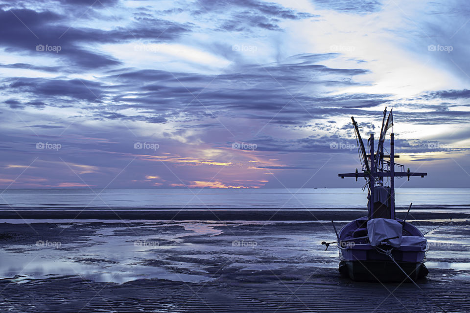 The morning sun light in the sea and the boat on the beach.