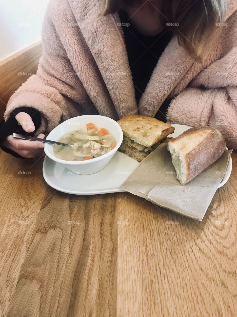 A teenage girl eating a bowl of chicken noodle soup with vegetables carrots and celery with a chicken chipotle avocado and tomato sandwich at panera bread restaurant located in USA, America 