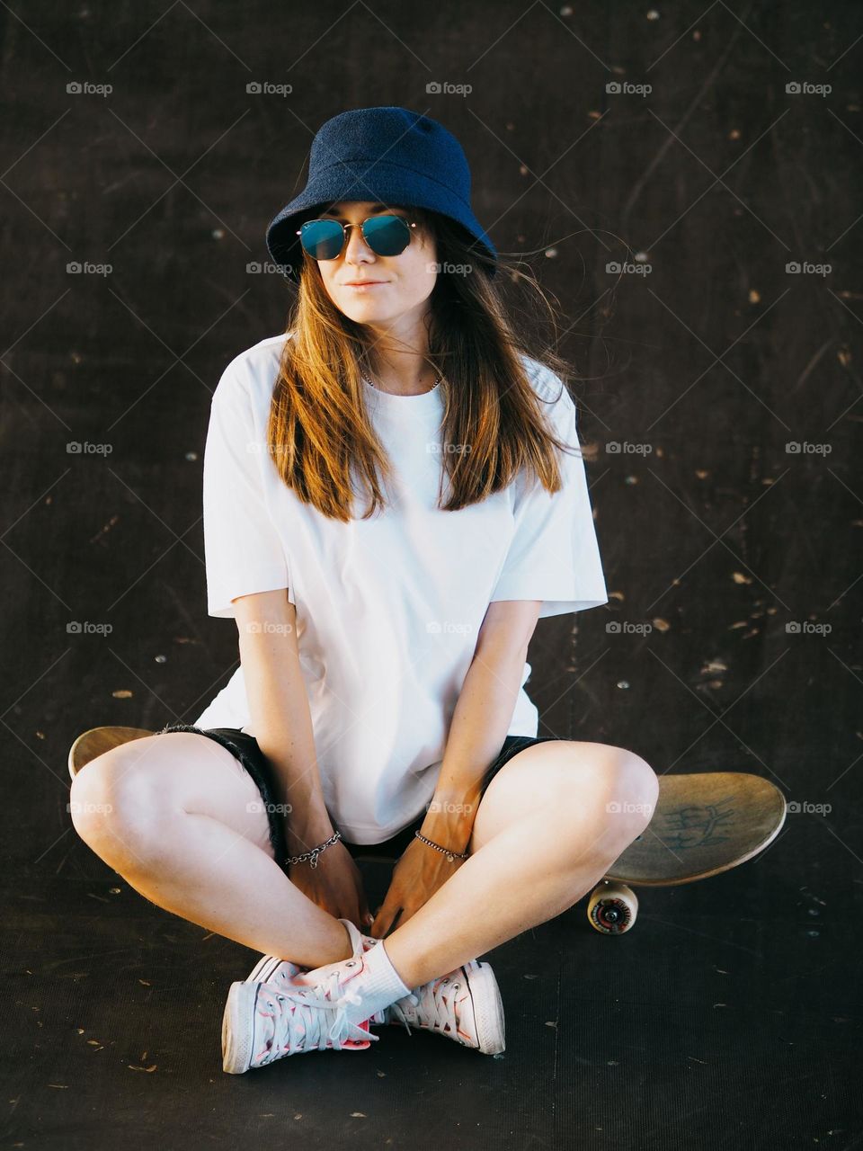 Young woman skater sitting on a skateboard in the street, portrait of woman 