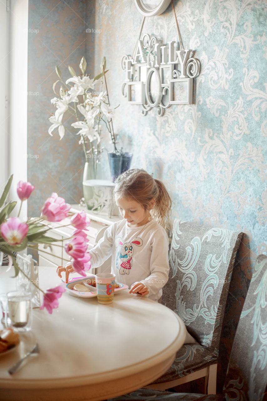 Little girl eating her breakfast in a light kitchen 