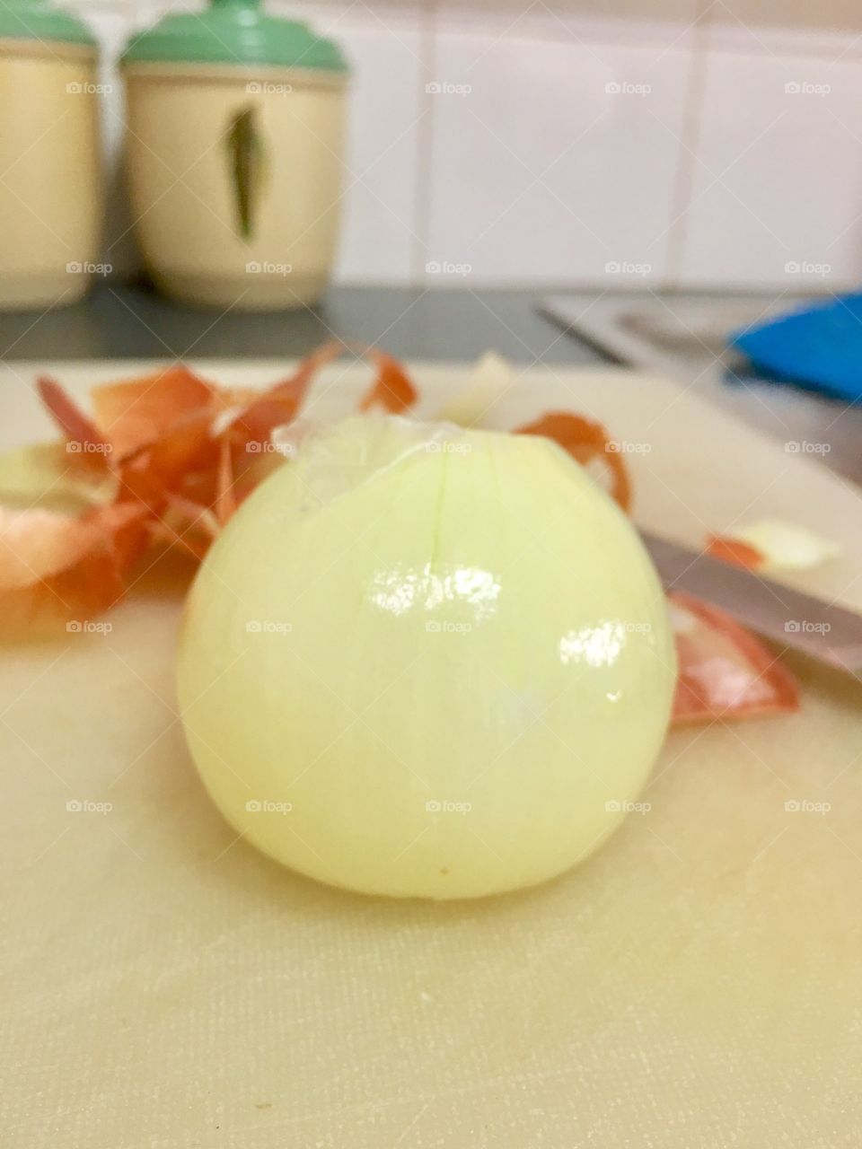 One peeled onion on white chopping board, peelings and knife in background closeup 