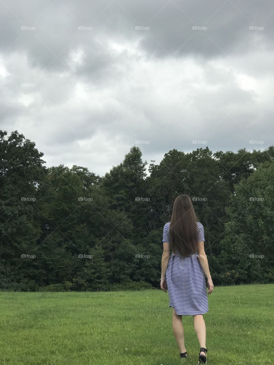 Girl walking towards woods in dress with long brunette hair