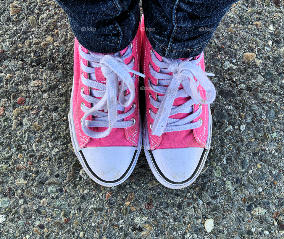 Looking down on Pink converse shoes on asphalt.