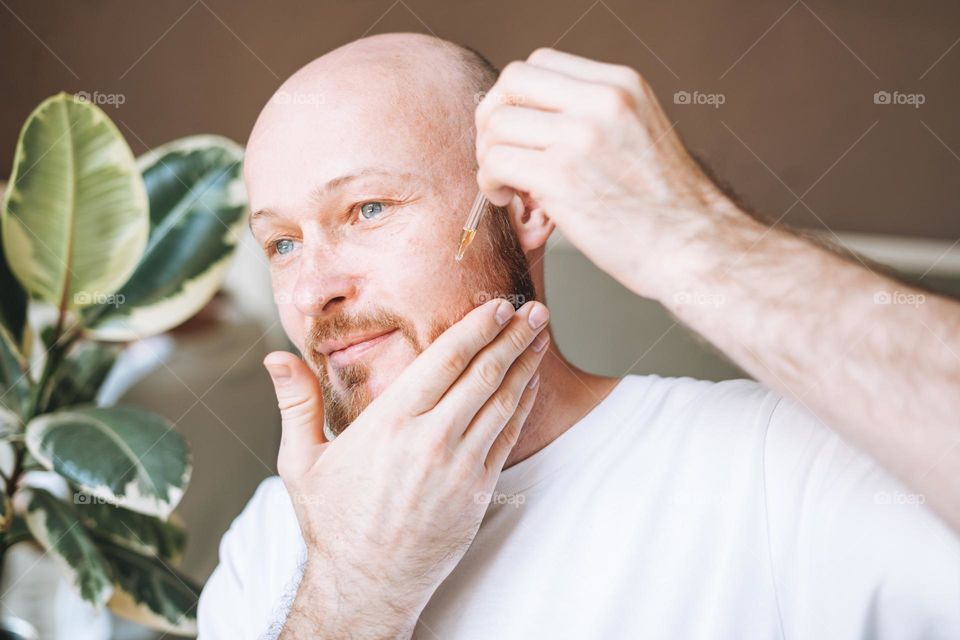 Adult handsome man with pipette with beard oil in bathroom at home