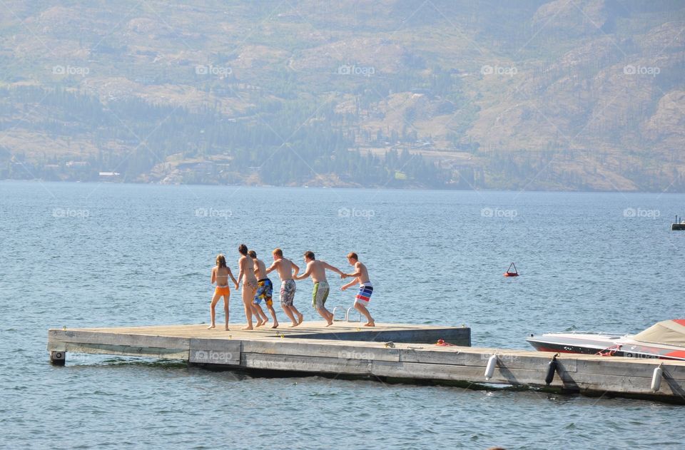 Group of young people running off dock into lake