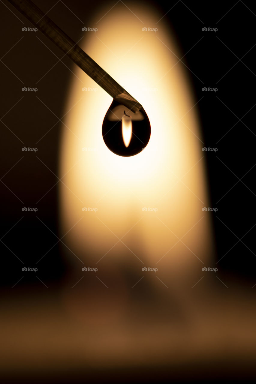 A macro portrait of a water drop in front of a candle's flame creating a silhouette of the droplet against the light of the flame and the candle of the flame and candle is refracted upside down in the drop.