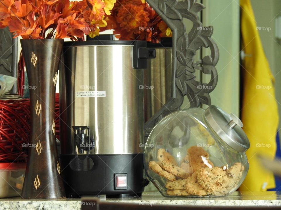 Orange yellow bouquet representing fall autumn behind a woven dark red basket perfect for autumn fall days to warm up with hot chocolate with a large capacity coffee brewer maker and a glass jar with cookies on a kitchen counter and mirror reflection