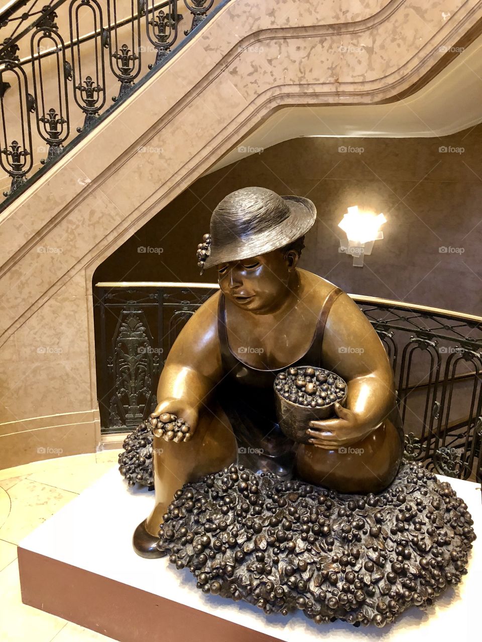 Metallic statue of chubby lady in swimsuit and summer hat holding a bucket and gathering berries