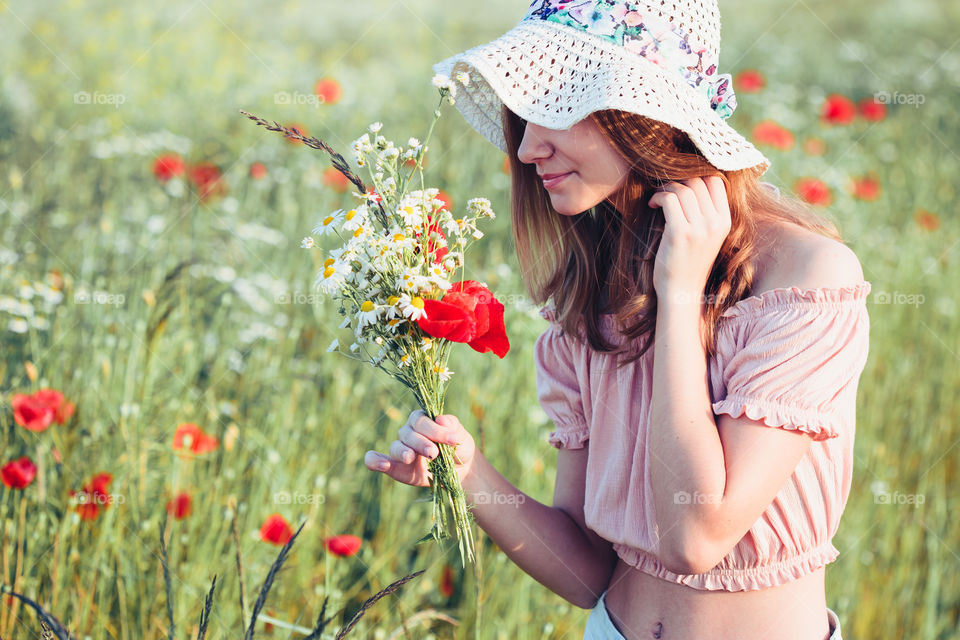 Beautieful young girl in the field of wild flowers. Teenage girl picking the spring flowers in the meadow, holding bouquet of flowers. She wearing hat and summer clothes. Spending time close to nature