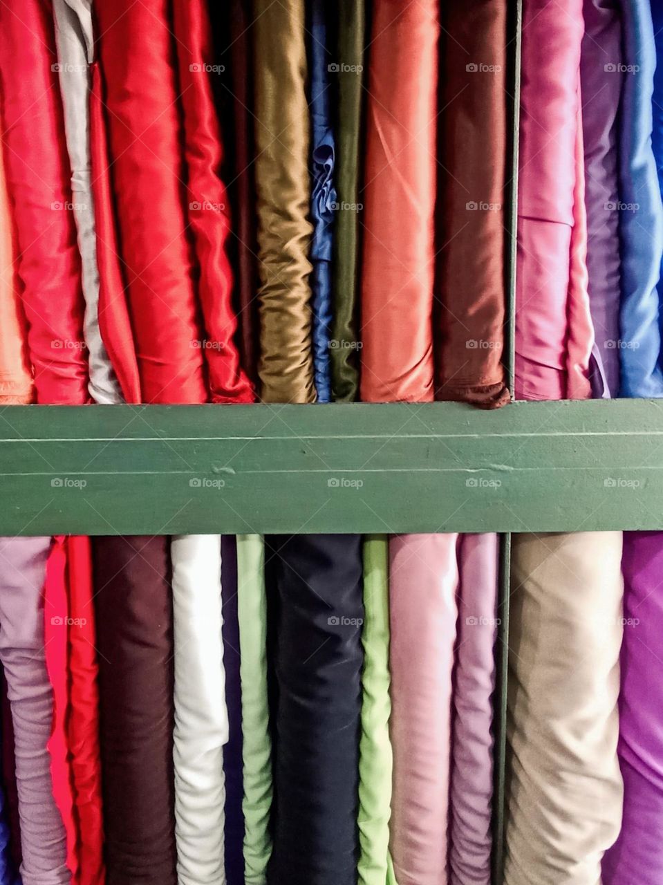 Close-up of a number of neatly arranged fabrics in various colors, placed on a shelf with a green wooden divider